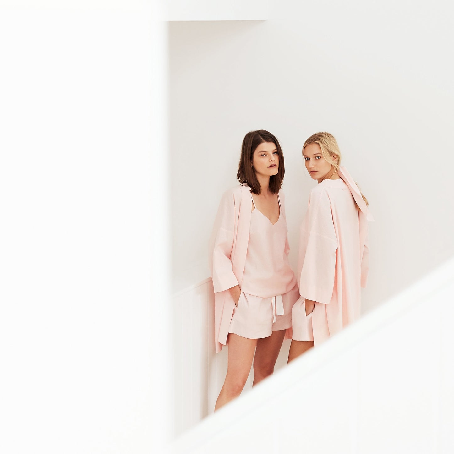 Two women wearing pink camis and shorts with robes