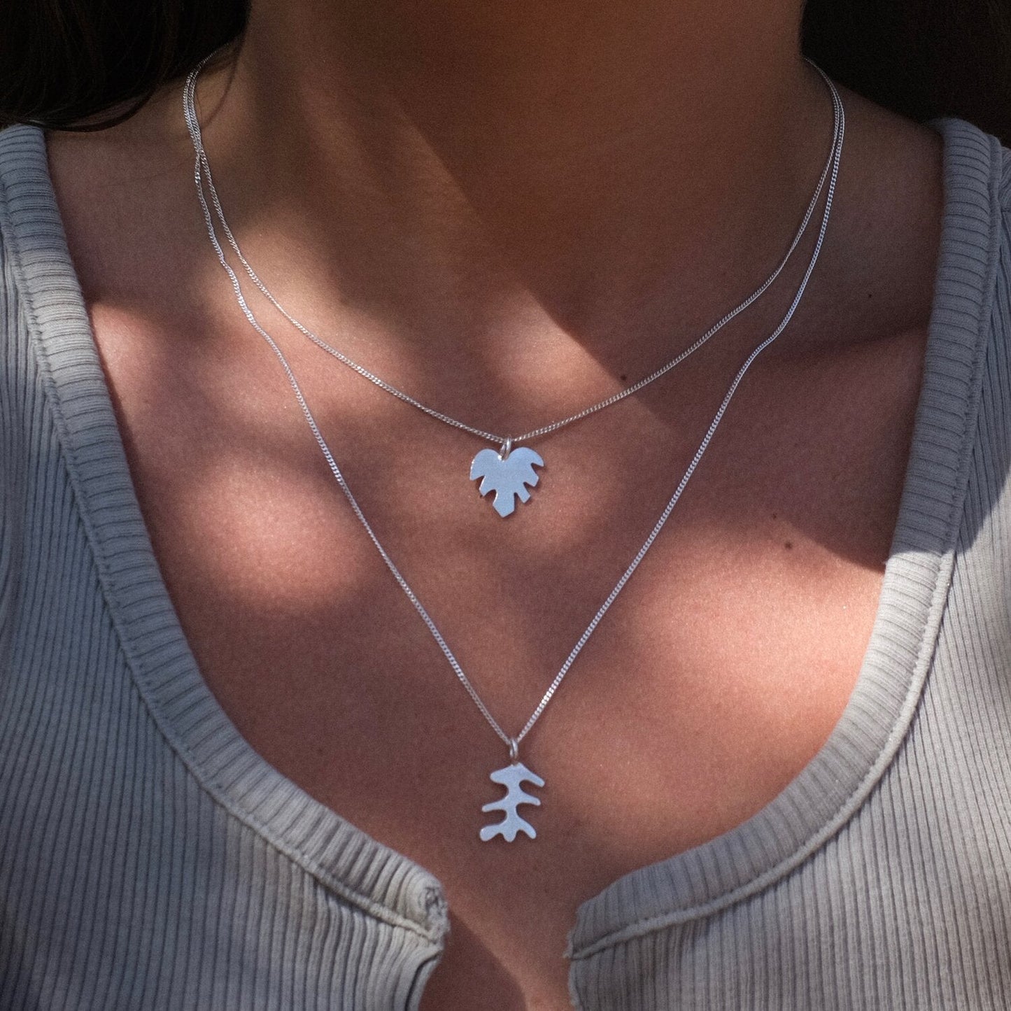 Close up of woman wearing pendant necklace with a silver leaf shape charm on it