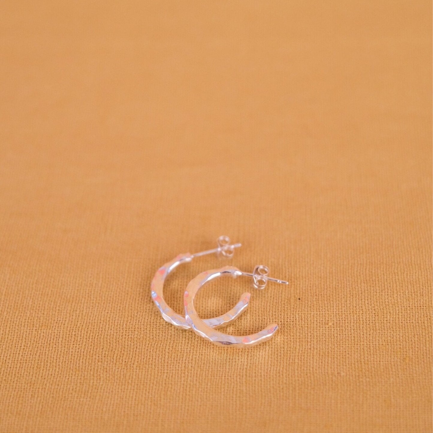 Close up of small silver hoop earrings with a textured surface
