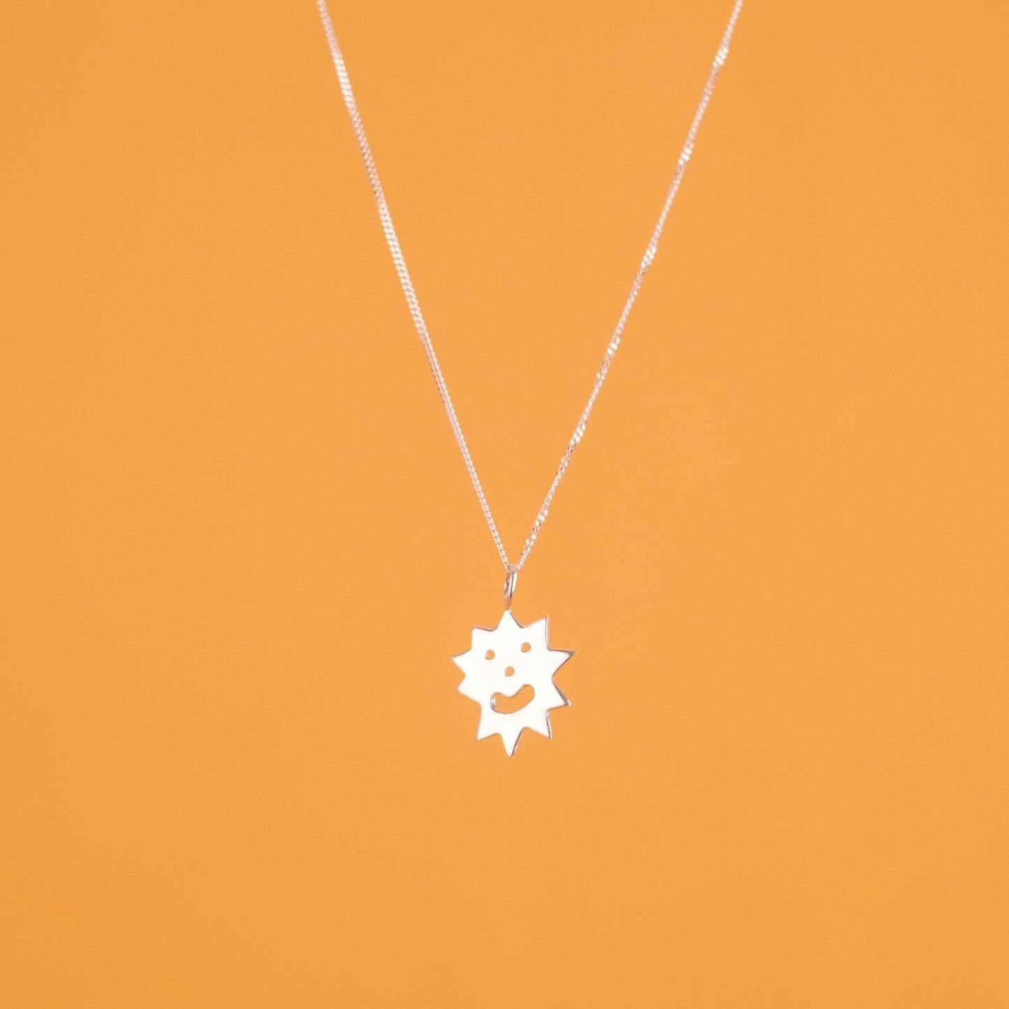 Close up of pendant necklace with a spiky irregular shaped charm with a smiley face on