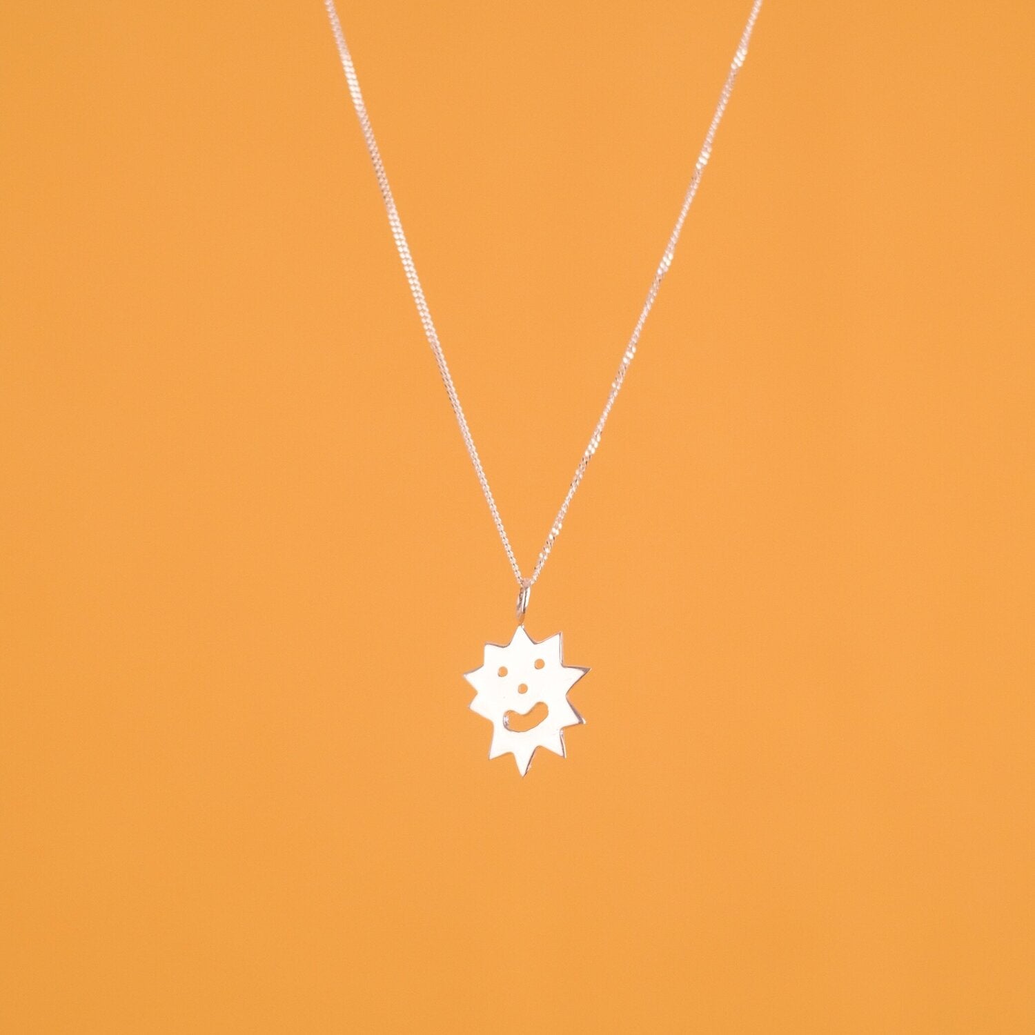 Close up of pendant necklace with a spiky irregular shaped charm with a smiley face on